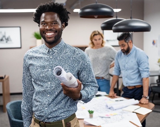 Black man holding rolled up paper with two people behind him